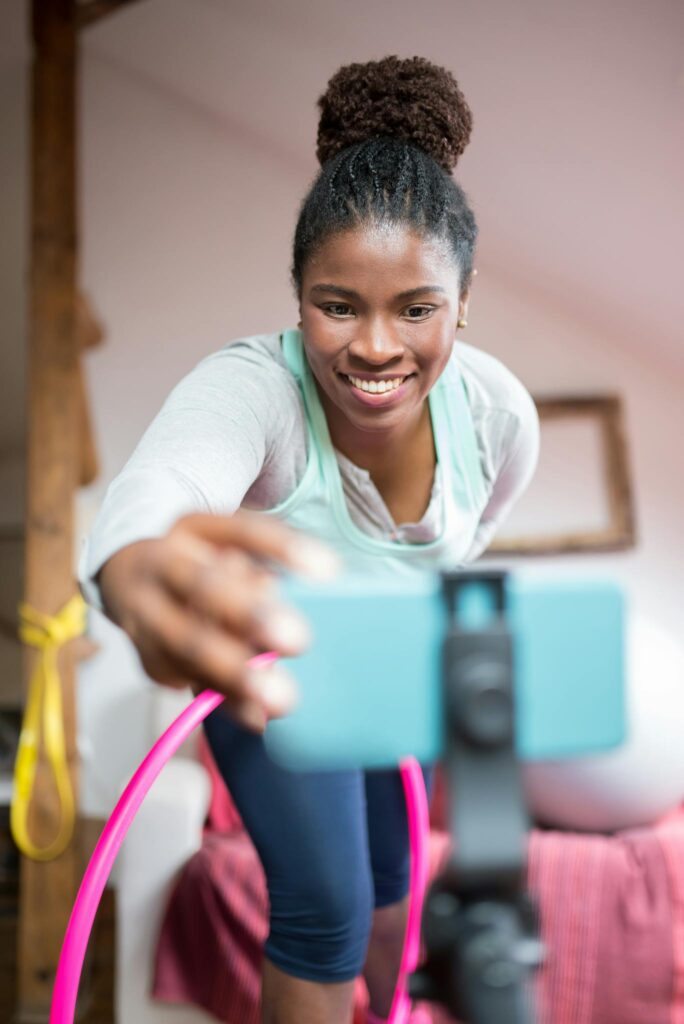 African American woman filming a fitness video with a smartphone indoors, smiling and engaged.